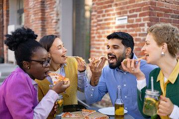 Group of friends joyfully eating pizza and drinks outdoors, enjoying a shared meal together at a restaurant or outdoor setting.