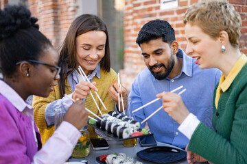 Diverse group of friends enjoys sushi and drinks together at an outdoor restaurant.