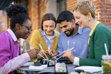 Diverse group of friends enjoying sushi together at an outdoor restaurant, sharing food and laughter.