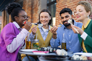 Diverse group of friends enjoying sushi and drinks outdoors, creating a relaxed and joyful dining experience.