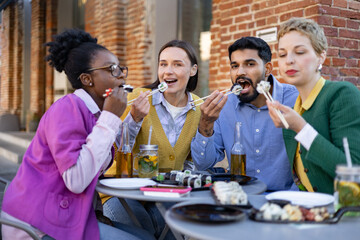 A diverse group of friends enjoys a meal of sushi together outdoors, laughing and eating.
