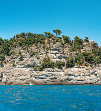 High-resolution photograph of the rugged coastline near Rapallo, close to Portofino in Liguria, Italy. The image features steep rocky cliffs covered in Mediterranean vegetation