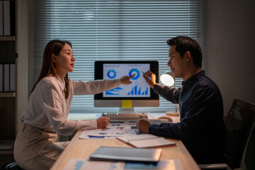 A man and a woman are sitting at a desk with a computer monitor in front of them