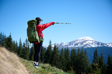Female hiker with backpack and trekking poles walking in the mountains. Adventure lifestyle in...