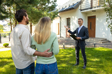 Real estate agent presenting modern house to couple in sunny yard