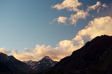 A night view of snowy mountains with clouds at sunset. The clouds and sky turn a magnificent golden color as the sun sets.