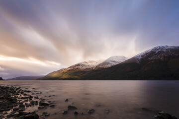 Schottischer Bergsee mit Spiegelung und verschneiter Gipfel unter dramatischem Himmel