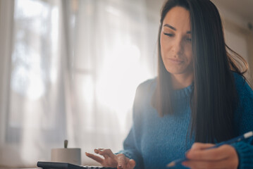 Focused accountant managing finances with calculator and pen in home office