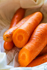 Close up image of fresh organic carrots, partially peeled, resting on a white kitchen towel in natural lighting. Vivid orange color, natural texture, and visible imperfections highlight authenticity
