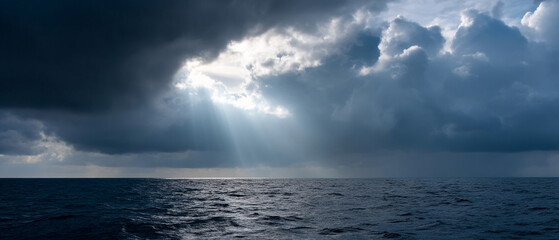 Fototapeta premium Sunlight streaming through dramatic storm clouds over calm ocean water, creating peaceful and moody atmosphere