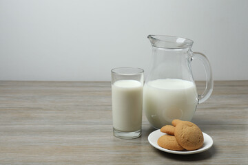 glass and jug with milk, cookies on wooden background