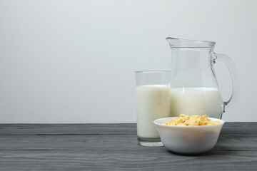 glass and jug with milk, cornflakes on grey wooden background
