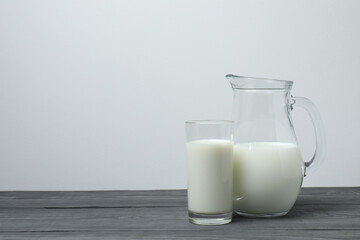 glass and jug with milk, on grey wooden background
