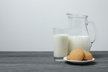 glass and jug with milk, cookies on grey wooden background