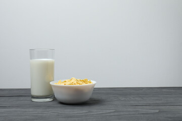 glass with milk, cornflakes on grey wooden background