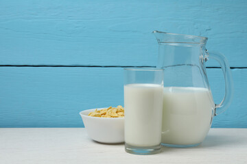 glass and jug with milk, cornflakes on white wooden background
