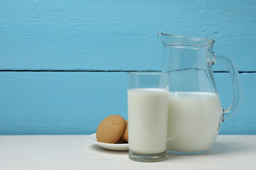 glass and jug with milk, cookies on white wooden background