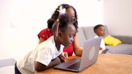 Young girl learning computer skills with maternal guidance, brother enjoying playful moment nearby in cozy home environment