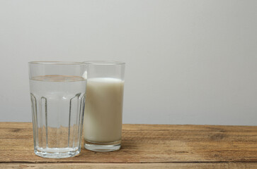 a glass full of milk and a glass of water on a wooden surface