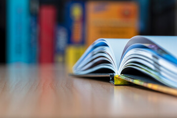 Open book lying on a desk with a blurred view of a bookshelf in the background, object with...