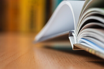 Open book lying on a desk with a blurred view of a bookshelf in the background, object with...