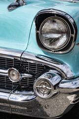 The headlamp and grill on an old turquoise car, with hood ornament on top.