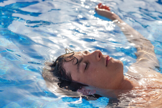 Teenage boy floating peacefully in crystal clear pool water, sunlight warming skin while experiencing serene summer moment - Powered by Adobe