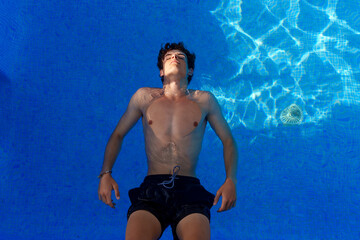 Serene male swimmer floating weightlessly, eyes closed, drifting in bright blue pool water during...