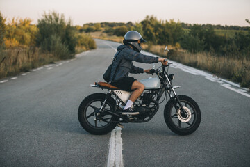 Young man riding custom motorcycle on country road