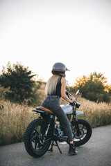 Fototapeta premium Young blonde woman riding custom motorcycle at sunset