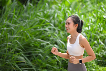 Fototapeta premium Fit Asian woman jogging among lush greenery under bright natural light