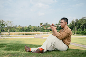 Outdoor portrait of male musician in casual attire enjoying trumpet music in nature