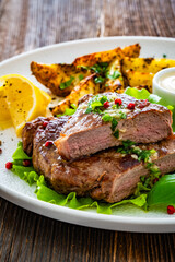 Grilled beef steak with baked potato wedges and fresh vegetables on wooden table	