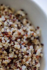 Macro image of freshly cooked tricolor quinoa with white, red, and black seeds in a white bowl. Healthy, gluten-free superfood rich in protein and texture.