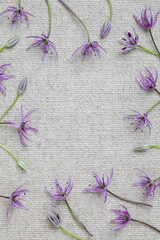 Flat lay of delicate purple wildflowers arranged in a circular frame on textured natural linen...