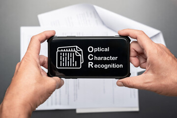 Hands holding smartphone displaying OCR Optical Character Recognition icon and text over a...