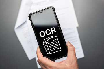 Hand holding smartphone with OCR icon over paper document, showing concept of Optical Character...