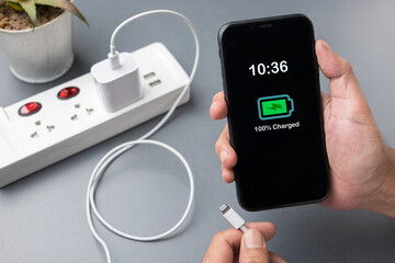 Person holding smartphone with 100% charged battery icon while unplugging USB cable from power...