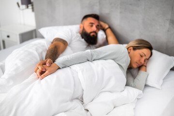 Young married couple is sleeping in their bed. They are holding hands and enjoying good sleep.