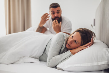 Couple is lying in bed and arguing. The woman is angry and offended and man is talking.