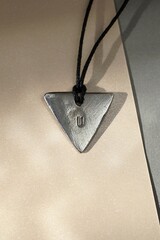 Artisanal Silver Triangle Pendant with Letter U on Black Cord in Sunlight. Unique Handmade Jewelry.