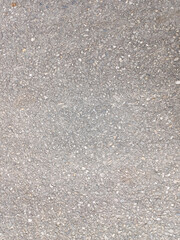 A close-up view of a grey, textured asphalt or concrete surface, revealing its granular composition and subtle variations in tone. Serves as a versatile background or texture, ideal for various design