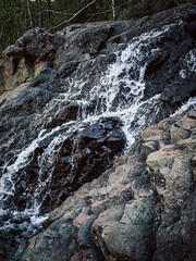 A waterfall is flowing down a rocky cliff. The water is clear and the rocks are grey. The scene is peaceful and serene