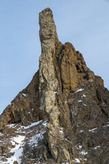 Towering rock formation rises sharply against a clear sky, showcasing rugged textures and snow-capped peaks, symbolizing the beauty of natural landscapes and geological wonders