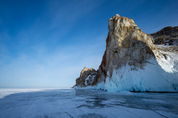 Majestic icy cliffs rise dramatically from frozen lake surface under clear blue sky, showcasing stunning natural beauty and serene winter landscape with reflections