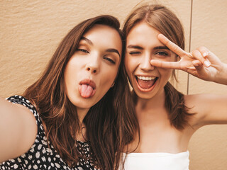 Two young smiling hipster women in summer clothes. Female taking selfie self portrait photos on...