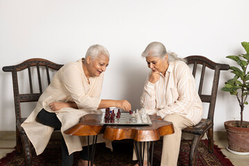 Two Indian senior woman caucasian friends or sisters play leisure chess board game at home have fun...