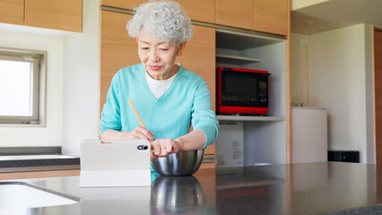 タブレットを見ながら料理するシニア女性