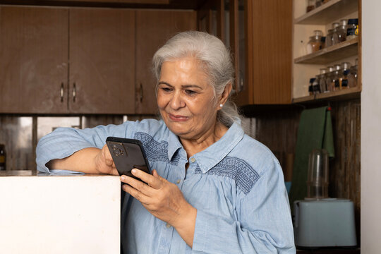 Indian happy active senior woman using 
smartphone at home