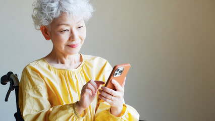 車椅子に乗ってスマホを使うシニア女性